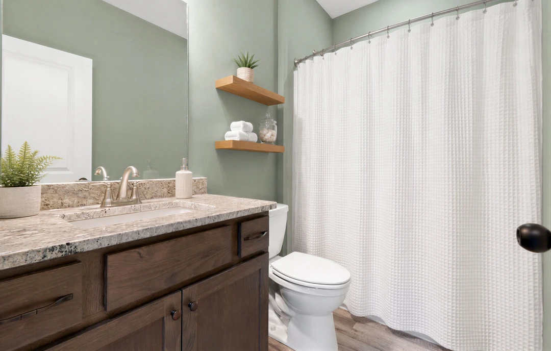 Bathroom with a white shower curtain, white toilet, light-colored countertop, bathroom cabinet, and a potted plant near a white door with green leaves.