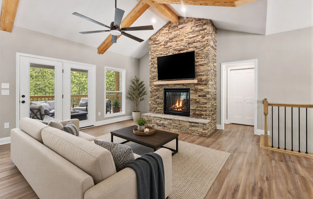 Living room with wood flooring, stone fireplace with a fire, ceiling fan, gray couch, television mounted on a stone wall, wooden railing with black bars, and a potted tree.