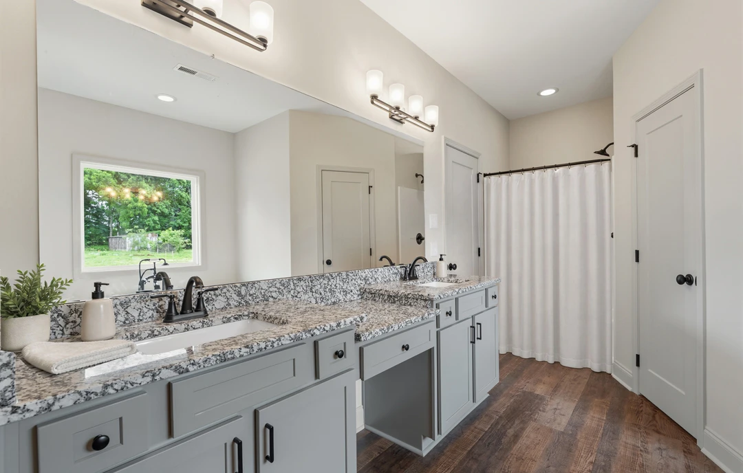 Bathroom with granite countertops, a white shower curtain, white cabinetry, a potted plant on the counter, a window showing trees outside, and a white door with a black knob.