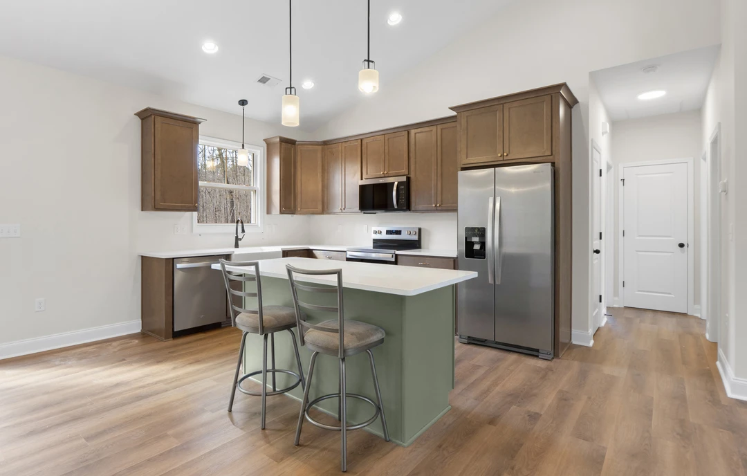 Kitchen with an island featuring granite countertops, white cabinetry, stainless steel refrigerator, microwave oven, bar stools, and laminate flooring.