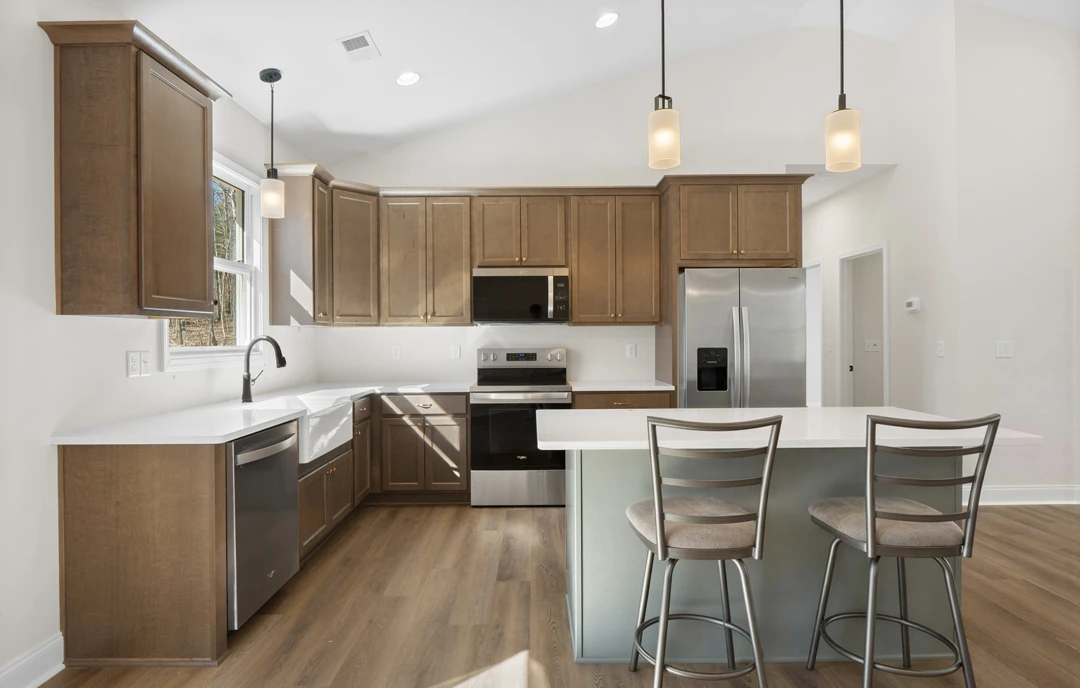 Kitchen with a bar area, stainless steel refrigerator, granite countertops, light cabinetry, built-in oven, and a cushioned chair at the counter.
