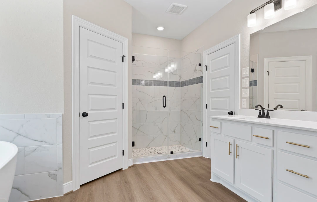 Bathroom with a glass shower featuring a black handle, white bathtub, white cabinetry, and tile flooring; a white door with a black knob is visible.