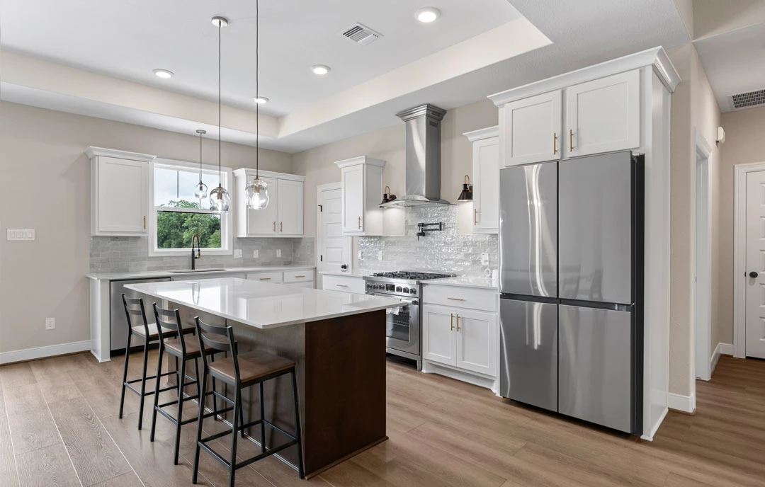 Kitchen with a large island featuring granite countertops, white cabinetry, stainless steel refrigerator and oven, bar seating with chairs, and light-colored flooring.