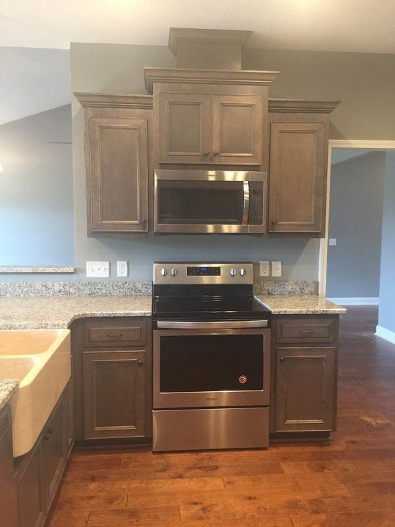 White kitchen cabinets with brushed nickel hardware, built-in stainless steel microwave above matching stove, light stone countertop, and brown wood door with silver handle