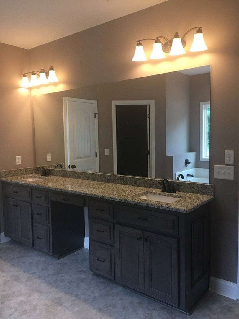 Bathroom featuring a marbled countertop with double sinks, expansive wall mirror, black door with white frame, white door with black hinges, and modern light fixture above the
