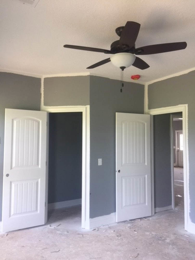 Ceiling fan with light fixture mounted on white ceiling above carpeted floor, flanked by white paneled doors with round knobs in a neutral-toned room