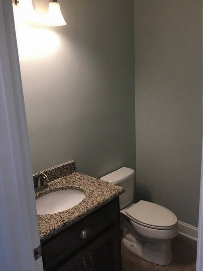 Marble countertop with white oval sink, chrome faucet, and adjacent white toilet in a tiled bathroom with wall-mounted mirror