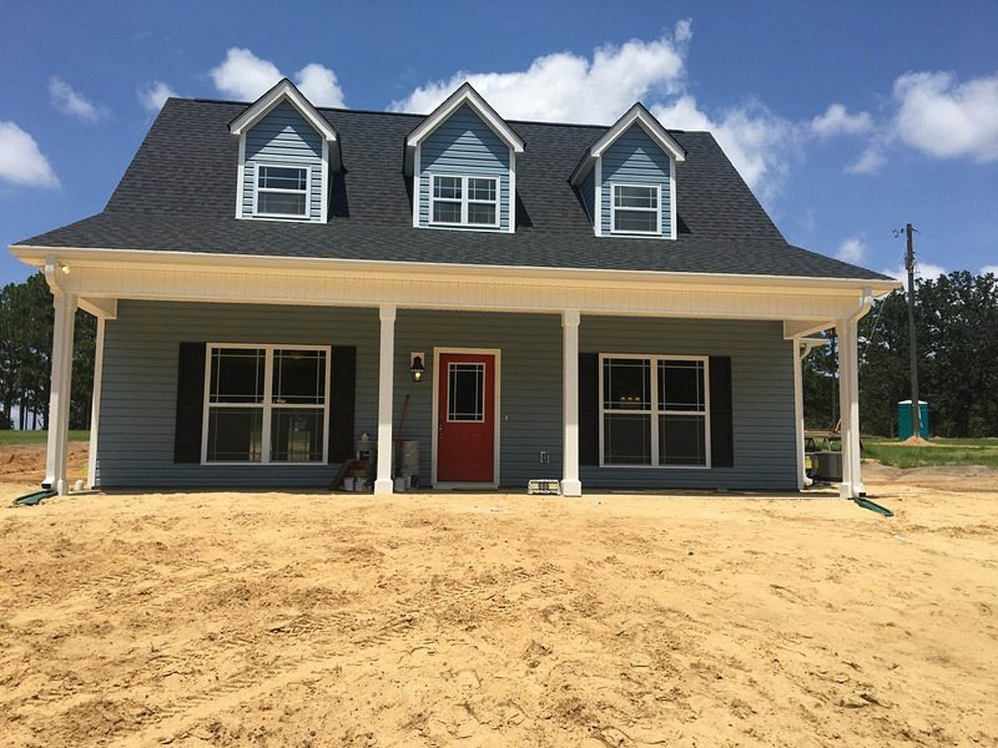 Two-story house with white siding, red front door with glass window, white-framed windows, dirt yard, and cloudy sky in background