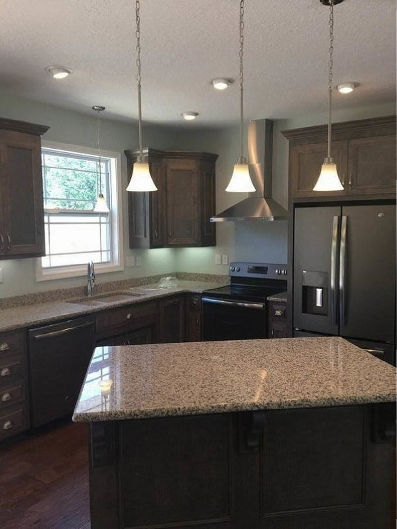 Granite countertops, black refrigerator, stove, cabinetry, sink, and pendant lighting in a modern kitchen.