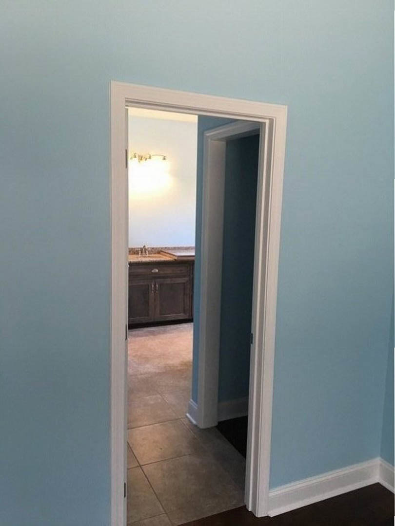 White-framed doorway leading to kitchen, tile floor, plaster walls, built-in cabinetry, bathroom mirror visible