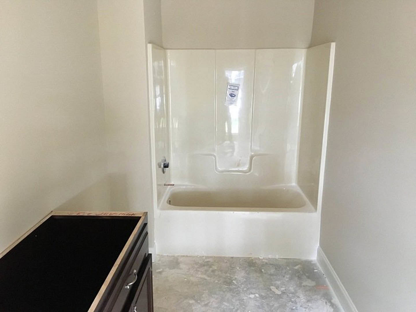 Freestanding white bathtub beside marble tile wall, modern sink with black rectangular vanity, grey tile flooring, white ceiling with recessed lighting