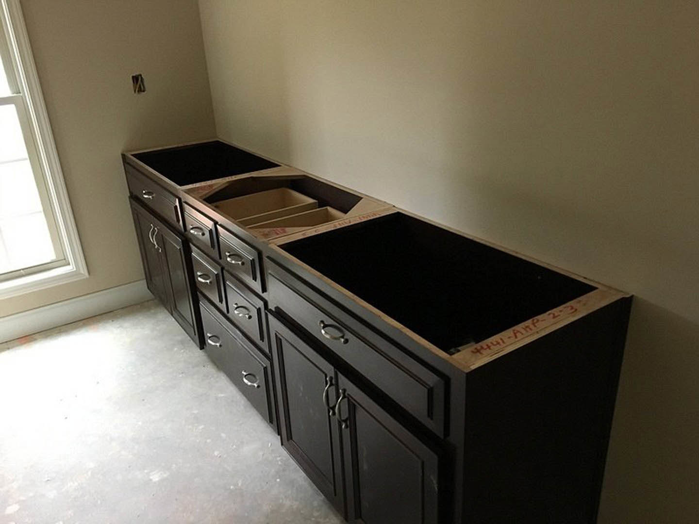 White kitchen counter with multiple drawers, black cabinetry, close-up of door handle, white door frame, and black box with red writing on top