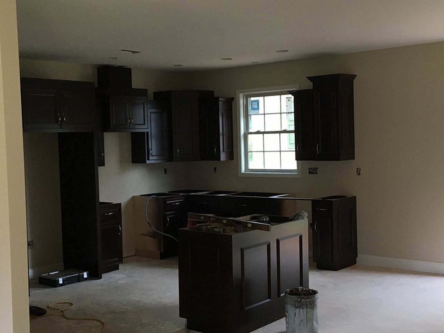 Kitchen with matte black cabinets, stainless steel handles, stone countertop, large window with a sign, grey trash can, and light-colored flooring