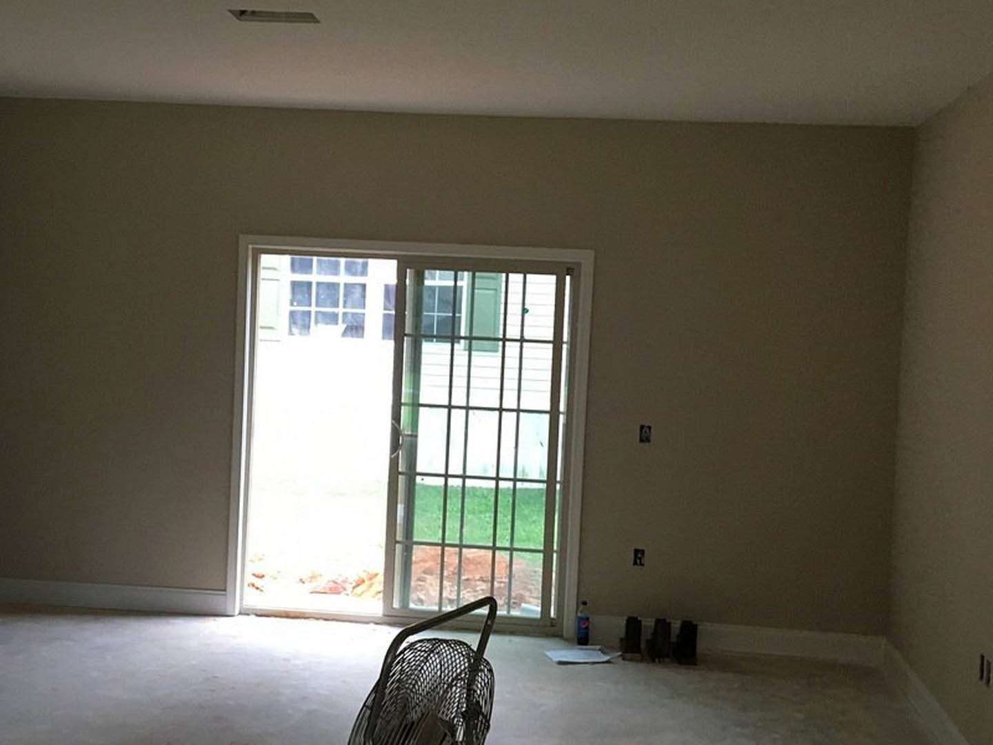Bright room with light wood flooring, white plaster walls, sliding glass door open to outside, metal basket with handle near a simple chair, net draped over chair back.