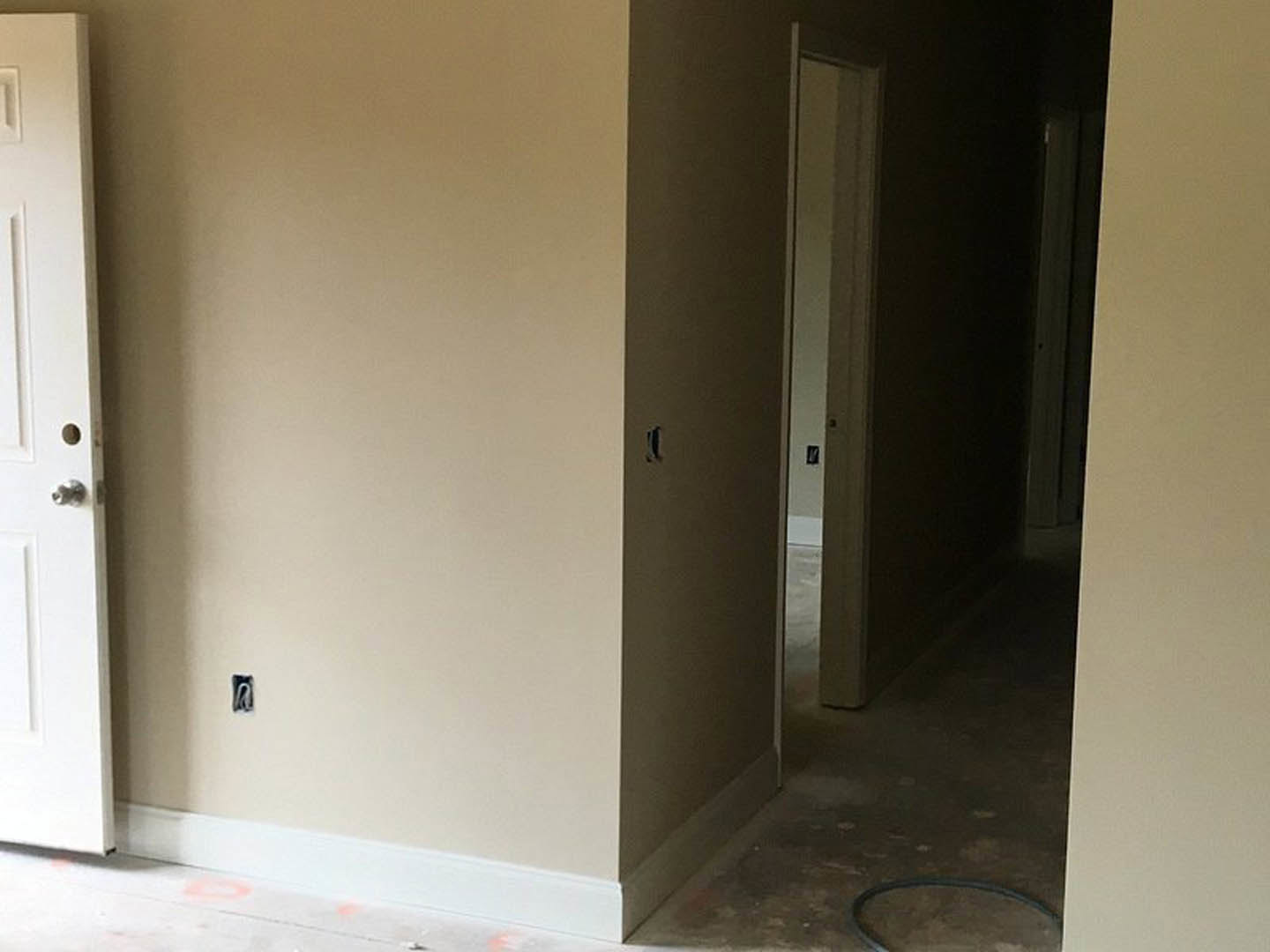 White hallway with light wood flooring, open white door featuring matte black handle, black curtain with white trim, smooth plaster walls, and visible door hardware.