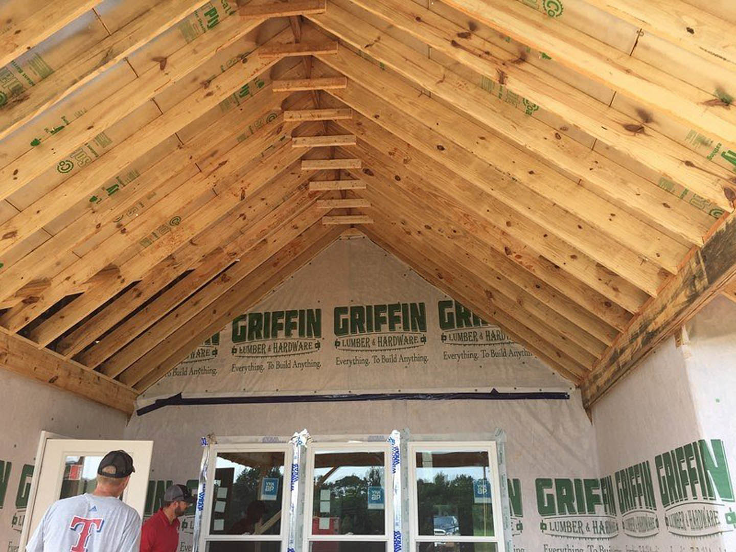 Wooden roof with exposed beams, two windows, and a person in a black baseball cap standing nearby; one window features a sign.