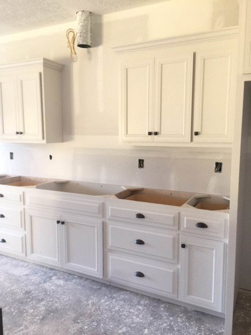 White shaker cabinets, light stone countertops, stainless steel sink with chrome faucet, tile backsplash, and recessed lighting in a modern kitchen.