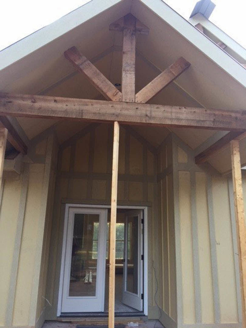 Partially constructed house exterior with exposed wooden beams, glass-paneled door, unfinished porch, and visible lumber framing