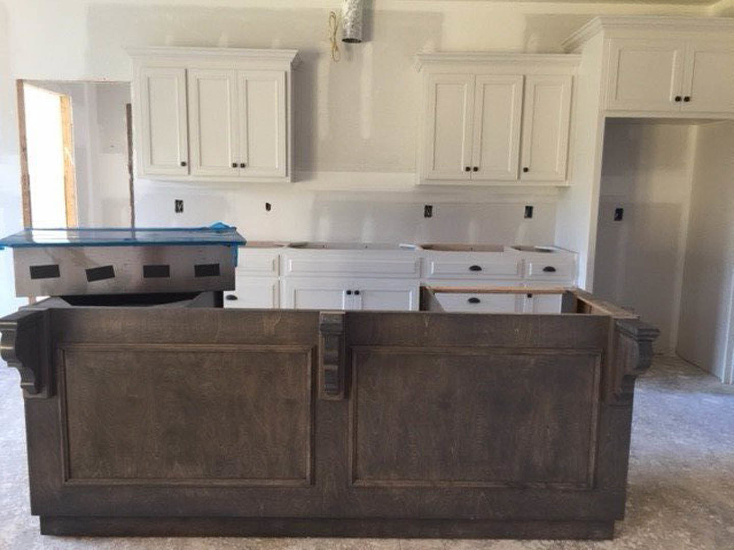 White kitchen cabinets with brushed metal handles, light stone countertops, stainless steel sink, and a built-in wood bench along the wall.