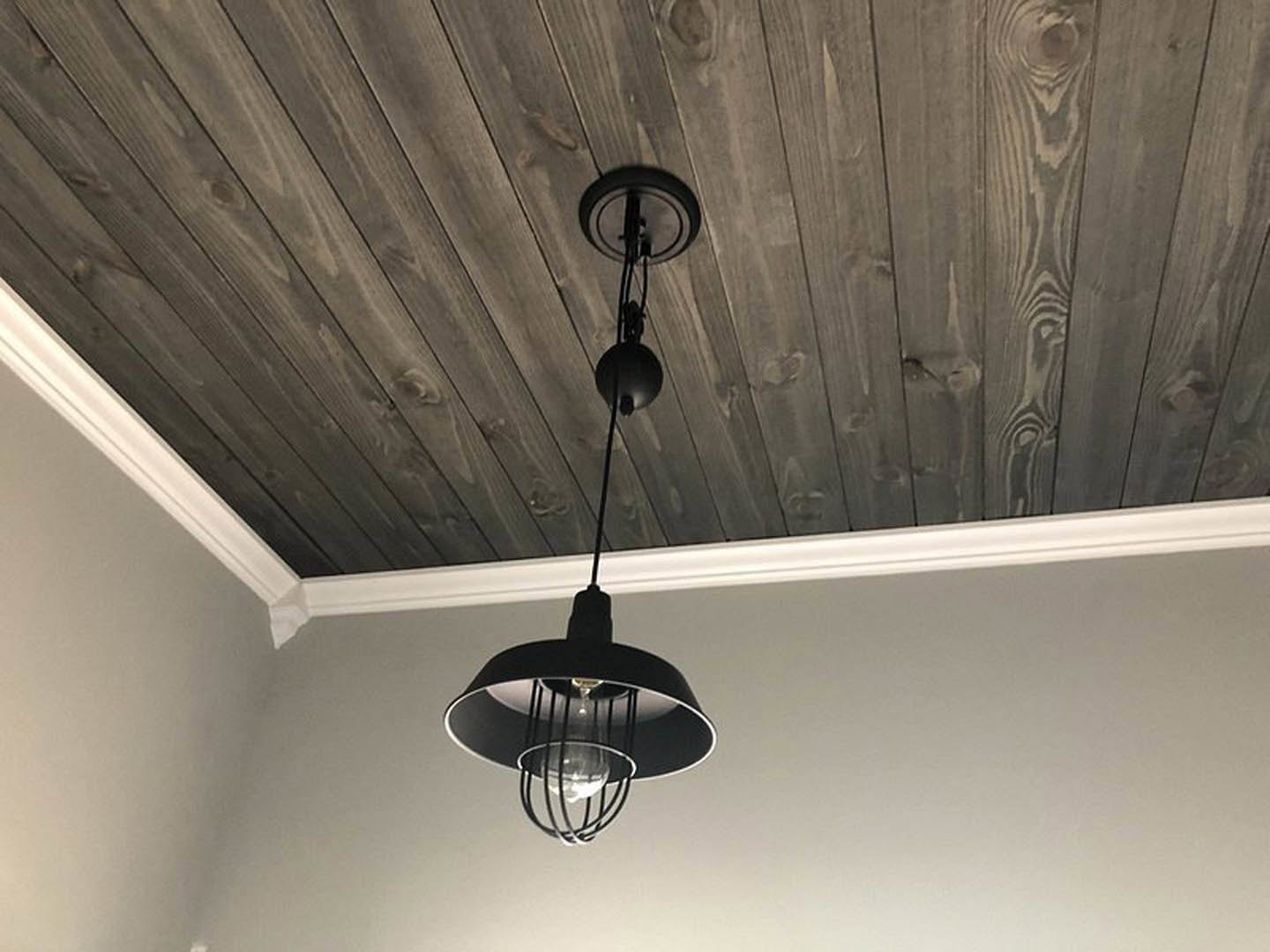 Black metal light fixture with exposed bulb mounted on warm-toned wooden ceiling in modern interior space
