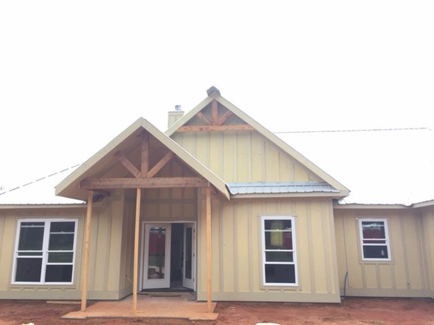 White-framed window and double glass-paneled door set in unfinished siding on custom home under construction, with roof and sky visible above