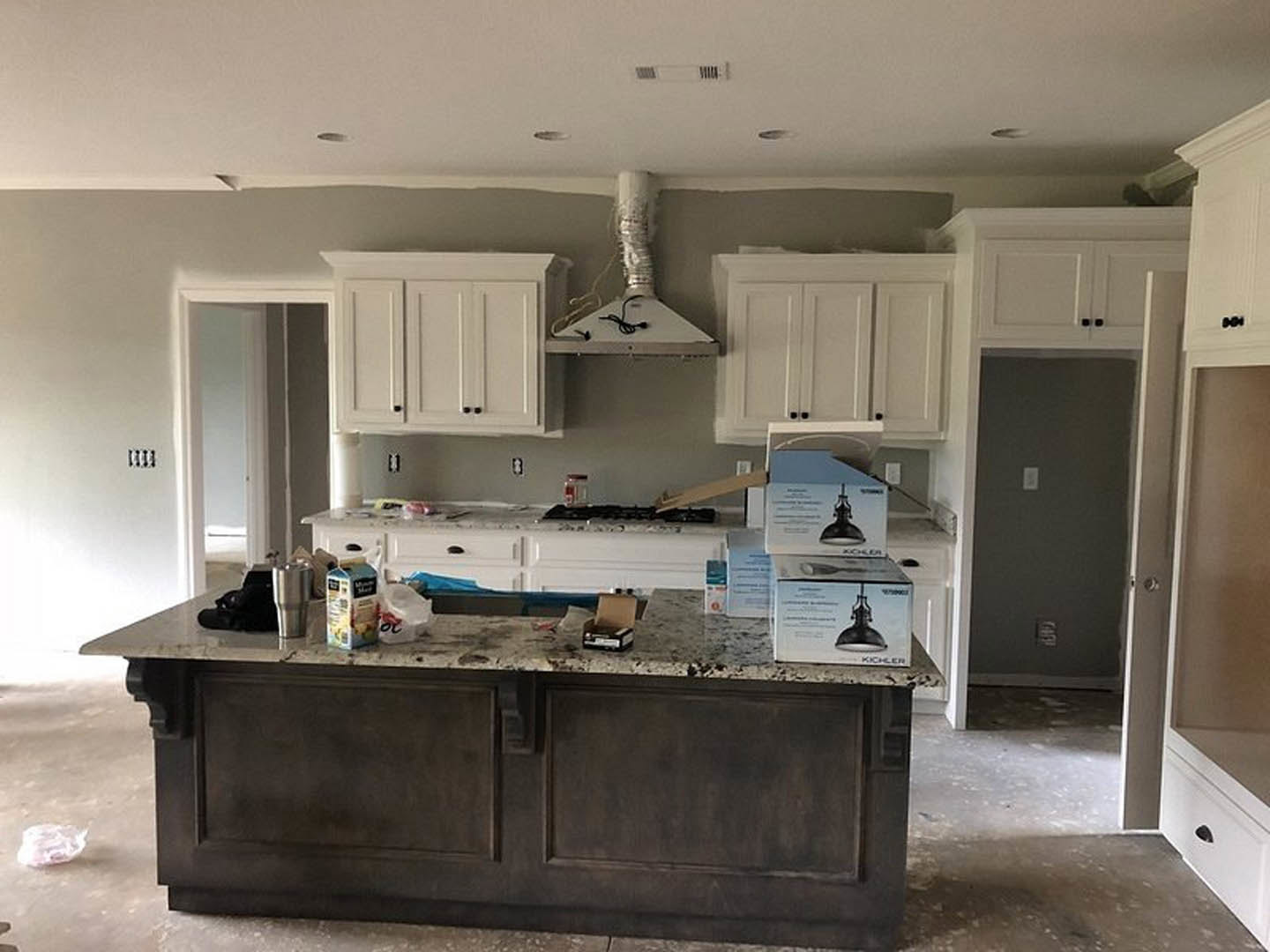 Spacious kitchen featuring a large marble island, white cabinetry, stainless steel vent hood, built-in appliances, and recessed lighting.