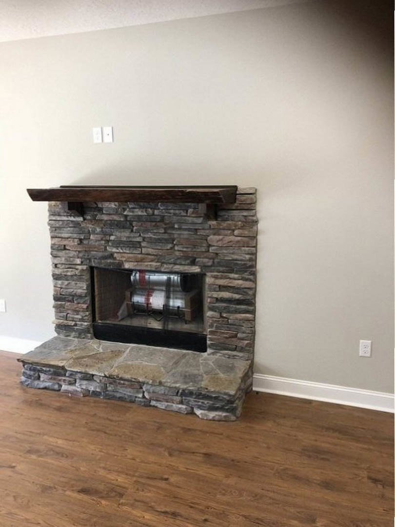 Stone fireplace with brick hearth and wooden mantel, wood floor, fire screen, and stone accent wall in a living room