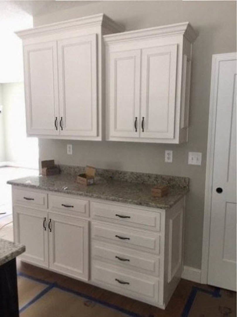White kitchen cabinets with black handles, marble countertop, white wall outlet with black buttons, white door with black knob, white dresser, and a blurry person’s leg in the