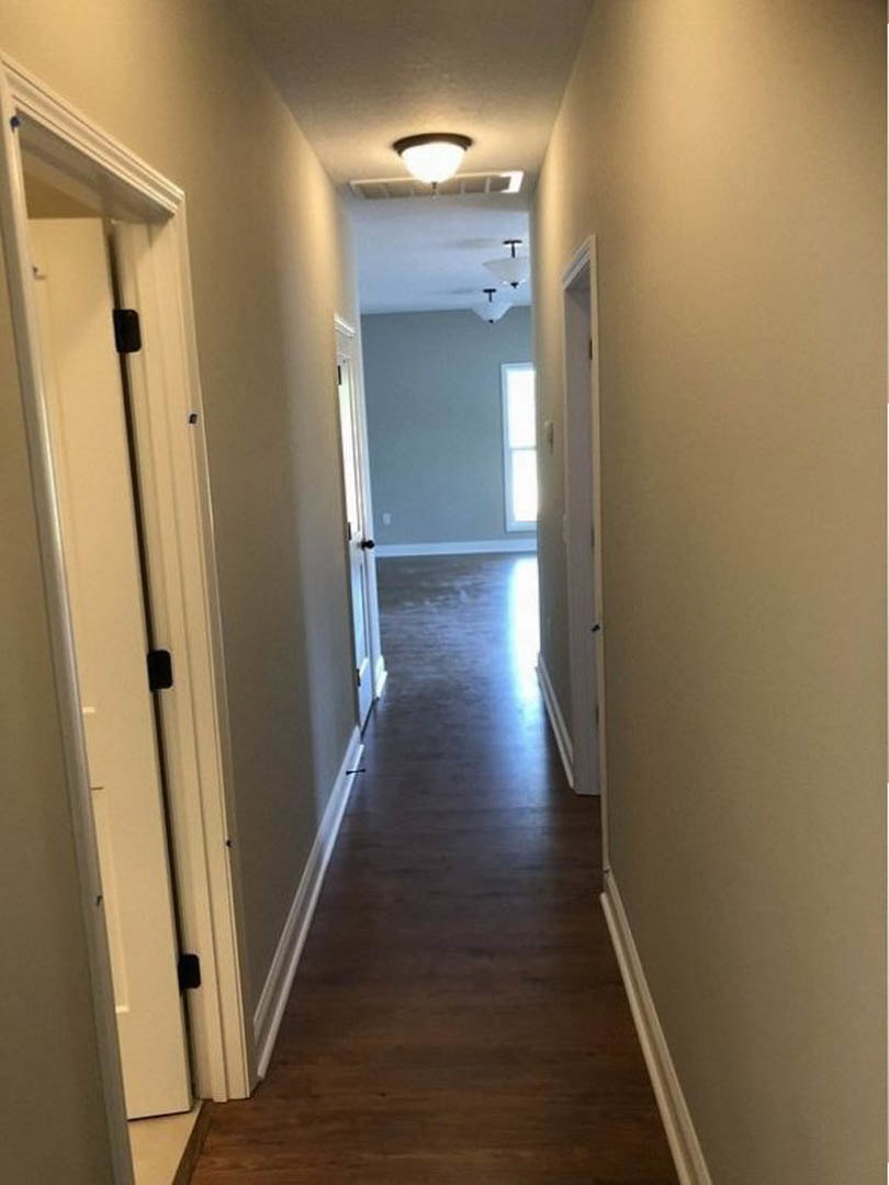 Hallway with warm wood flooring, white walls, brown door frame, round ceiling light fixture, and blue accent wall featuring a window
