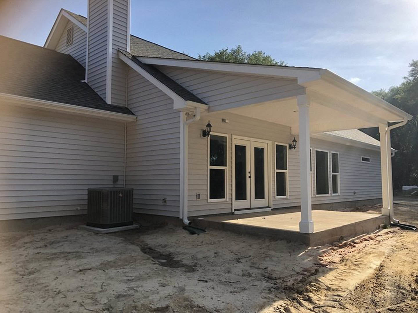 Two-story home with white siding, covered front porch supported by columns, large patio area, white-framed windows, black door, and landscaped yard.
