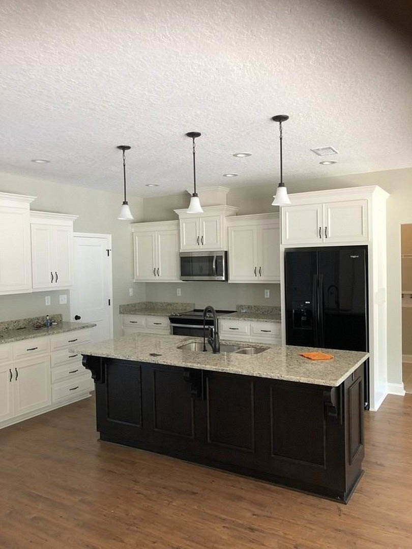 Kitchen with black and white island featuring built-in sink, black cabinets, wooden flooring, microwave oven with handle, napkin on countertop, and white wall with black border.