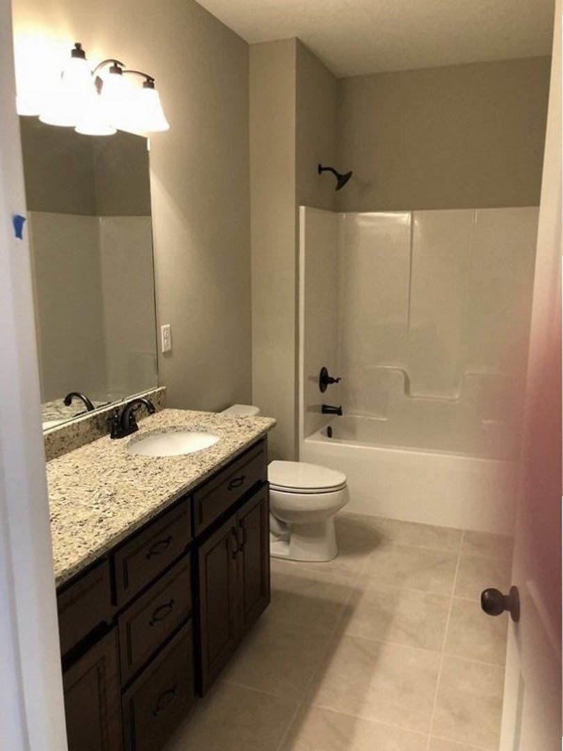 Modern bathroom featuring a white ceramic sink with chrome faucet, glass-enclosed shower with tiled walls, light wood cabinetry, and neutral tile flooring