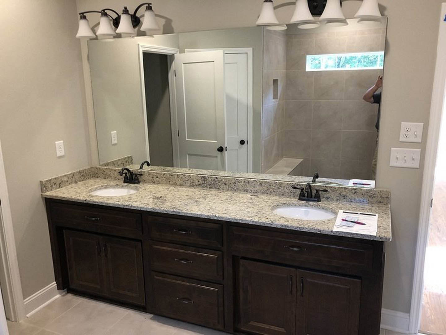 Bathroom with expansive mirror above a stone countertop, modern faucet, white cabinetry with drawers, and tiled walls