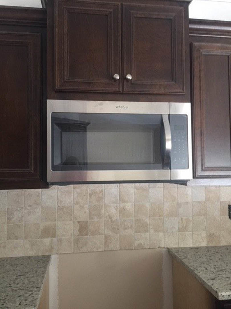 Granite countertop with built-in microwave above, white cabinetry and tiled backsplash visible