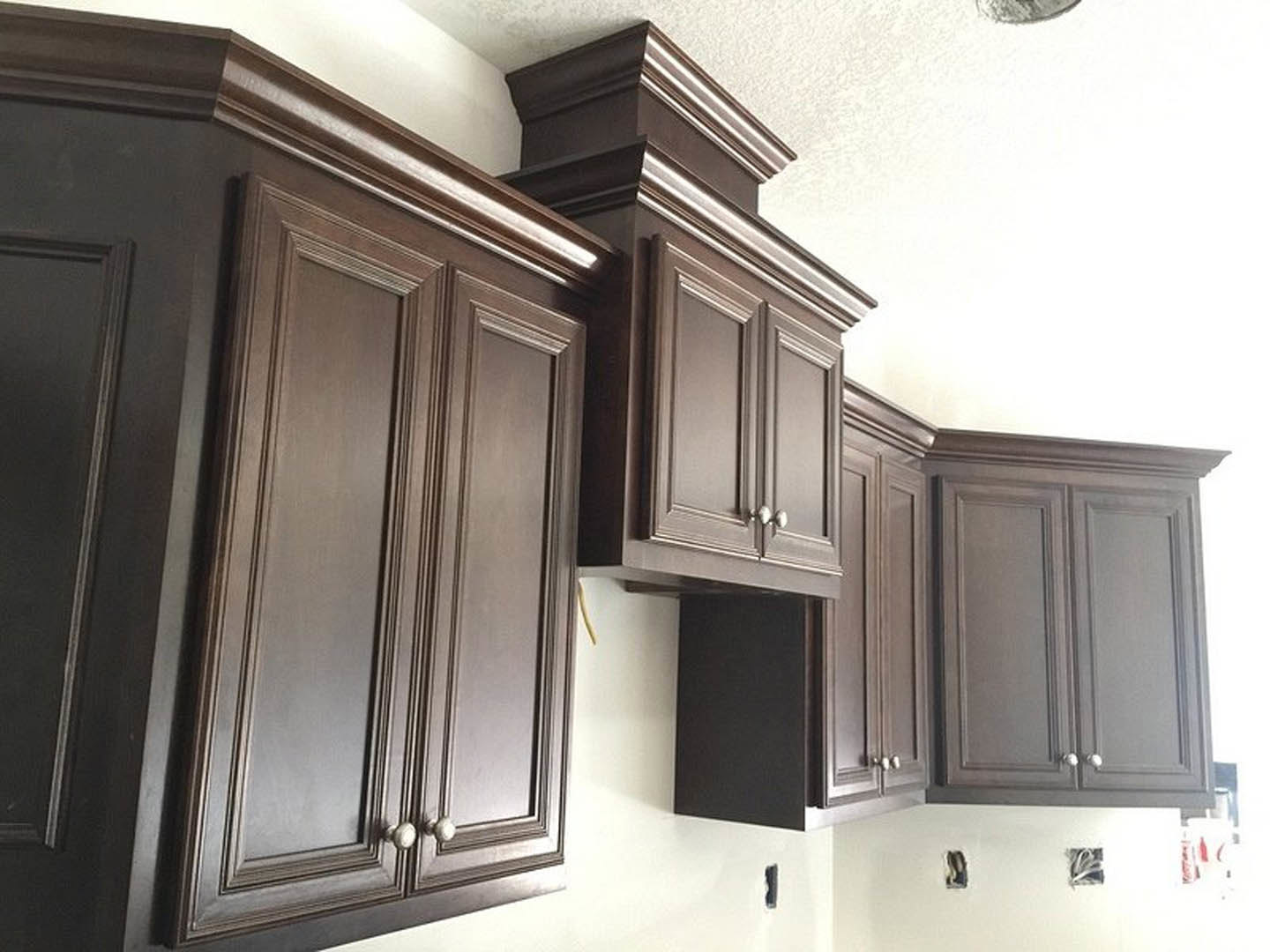 Dark wood kitchen cabinets with sleek black hardware, white countertop, and integrated appliances in a modern interior.