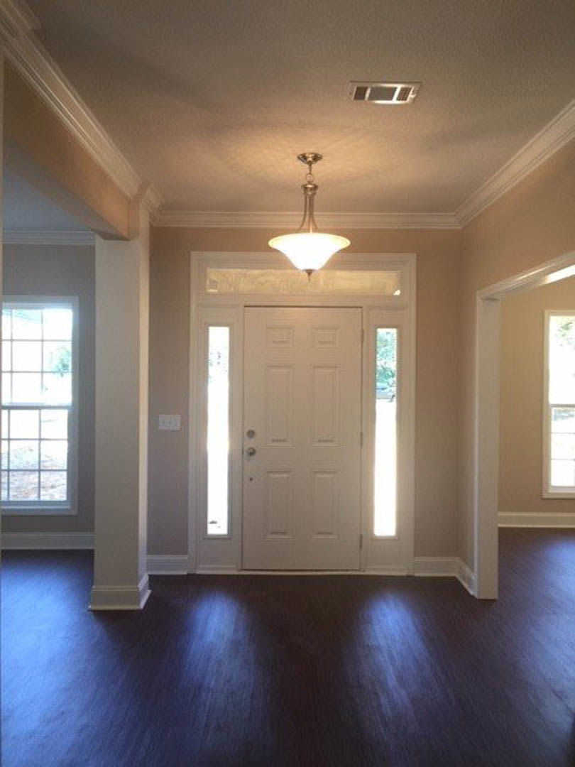 Close-up of a modern ceiling light fixture above dark hardwood flooring, white door with silver handle and two windows, white window frames, and crisp white wall molding
