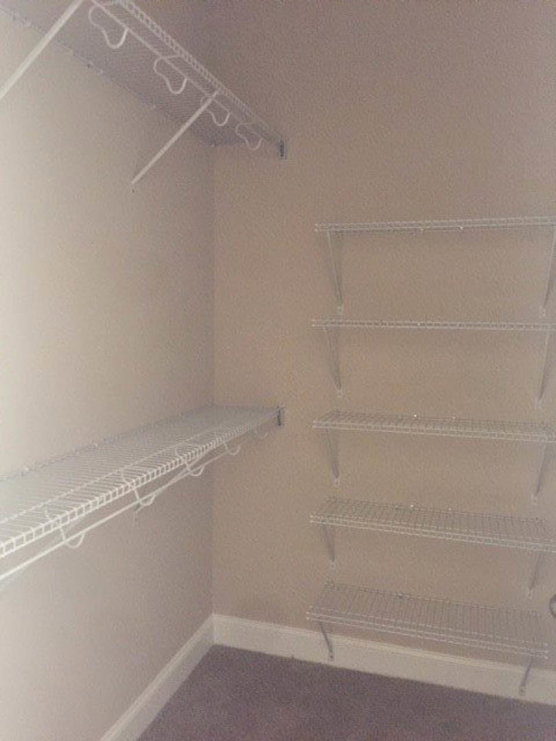 Walk-in closet with white wire shelving, beige carpet flooring, and smooth plaster walls