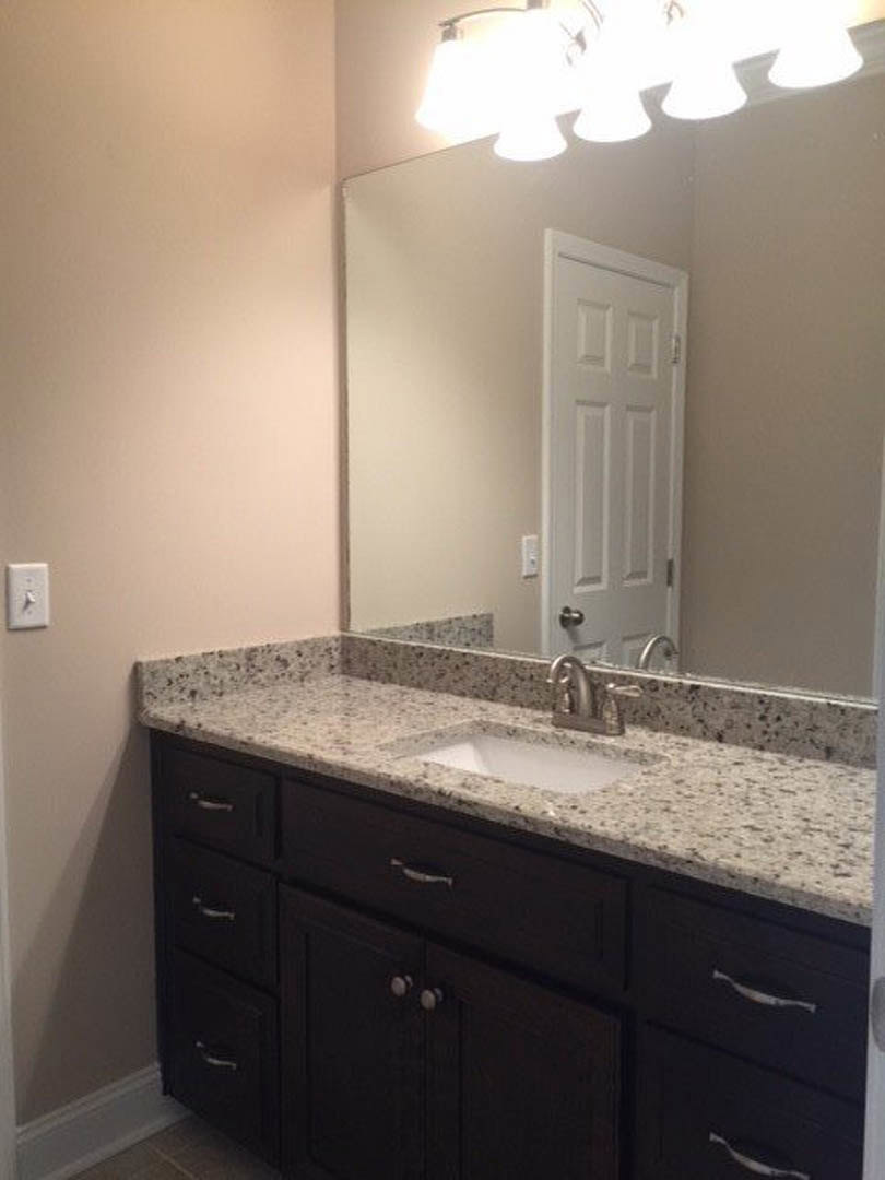 Modern bathroom featuring a white countertop sink, chrome faucet, large rectangular mirror, light gray tile backsplash, and sleek cabinetry with drawers.