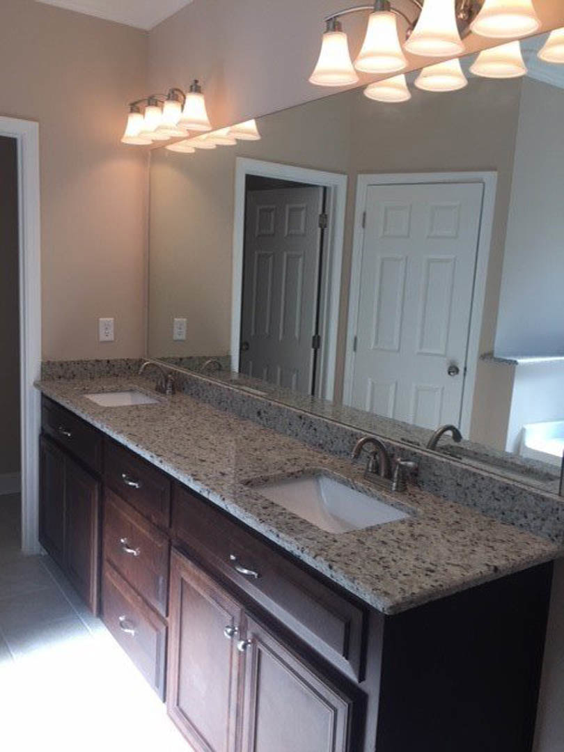 Bathroom with two rectangular white sinks set in a stone countertop, large framed mirror above, modern silver faucets, white cabinetry with drawers, overhead light fixture
