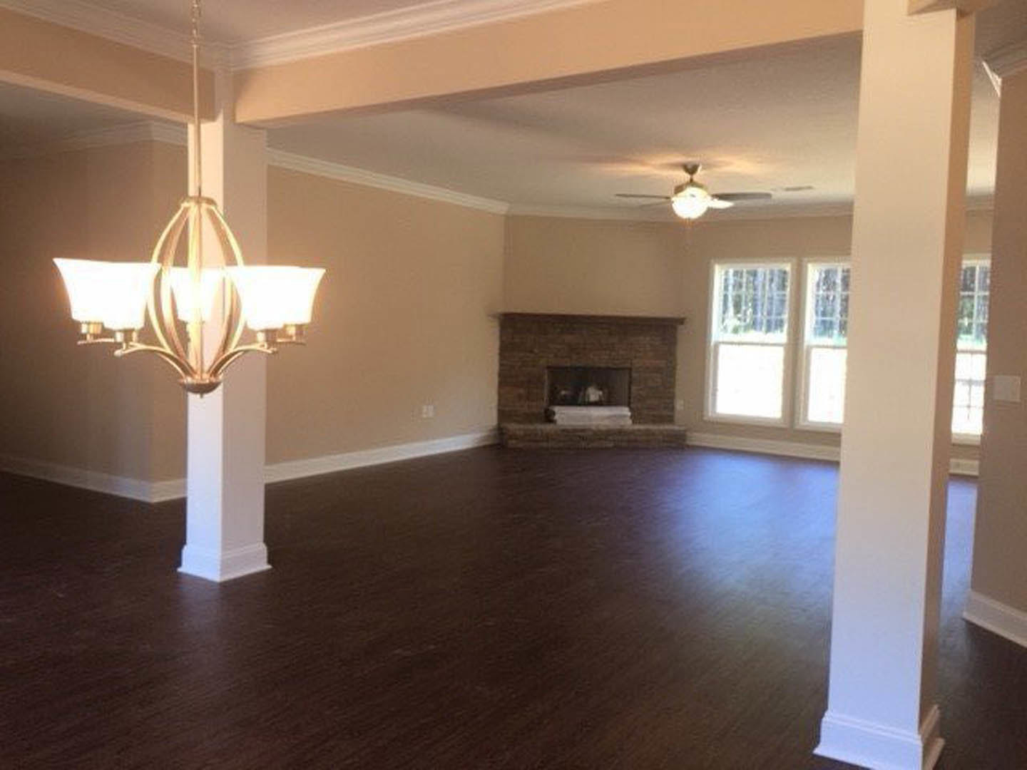 Living room with hardwood floors, brick fireplace, three-lamp chandelier, white-framed window, and crown molding on ceiling