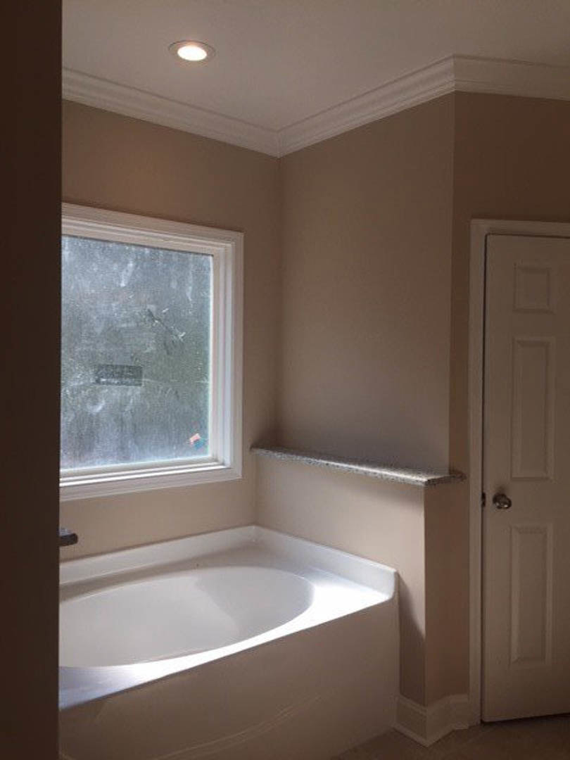 White freestanding bathtub with sunlight highlighting the rim, set against plaster walls near a window and chrome tap in a modern bathroom.