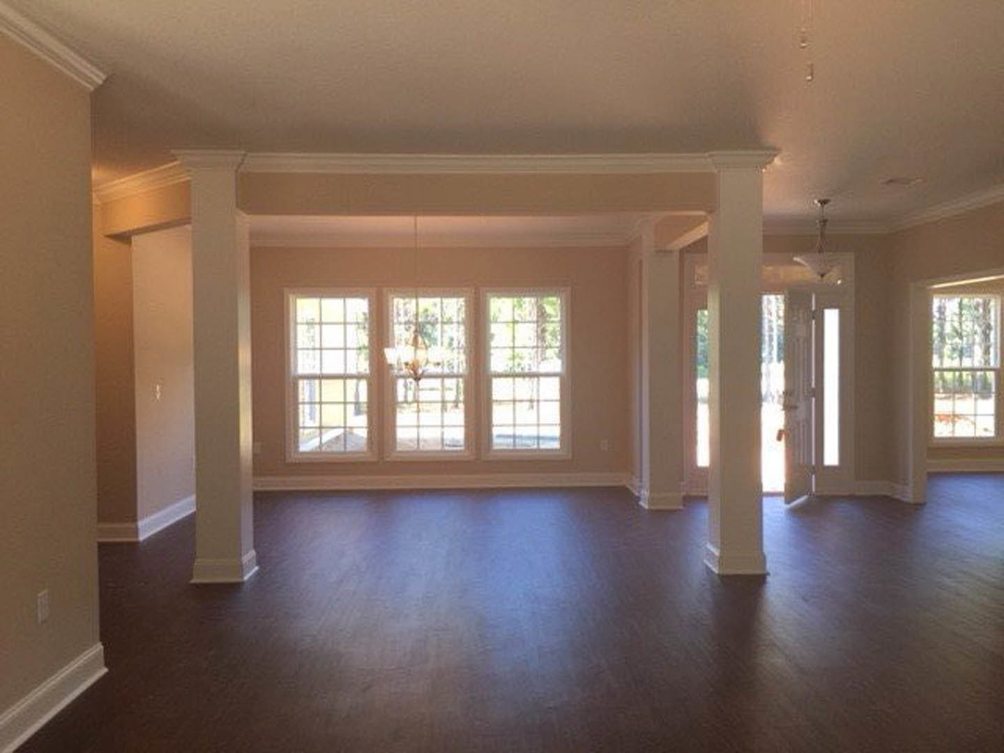 Dark wood flooring, white paneled door, large windows with white frames, chandelier hanging from ceiling, view of trees outside
