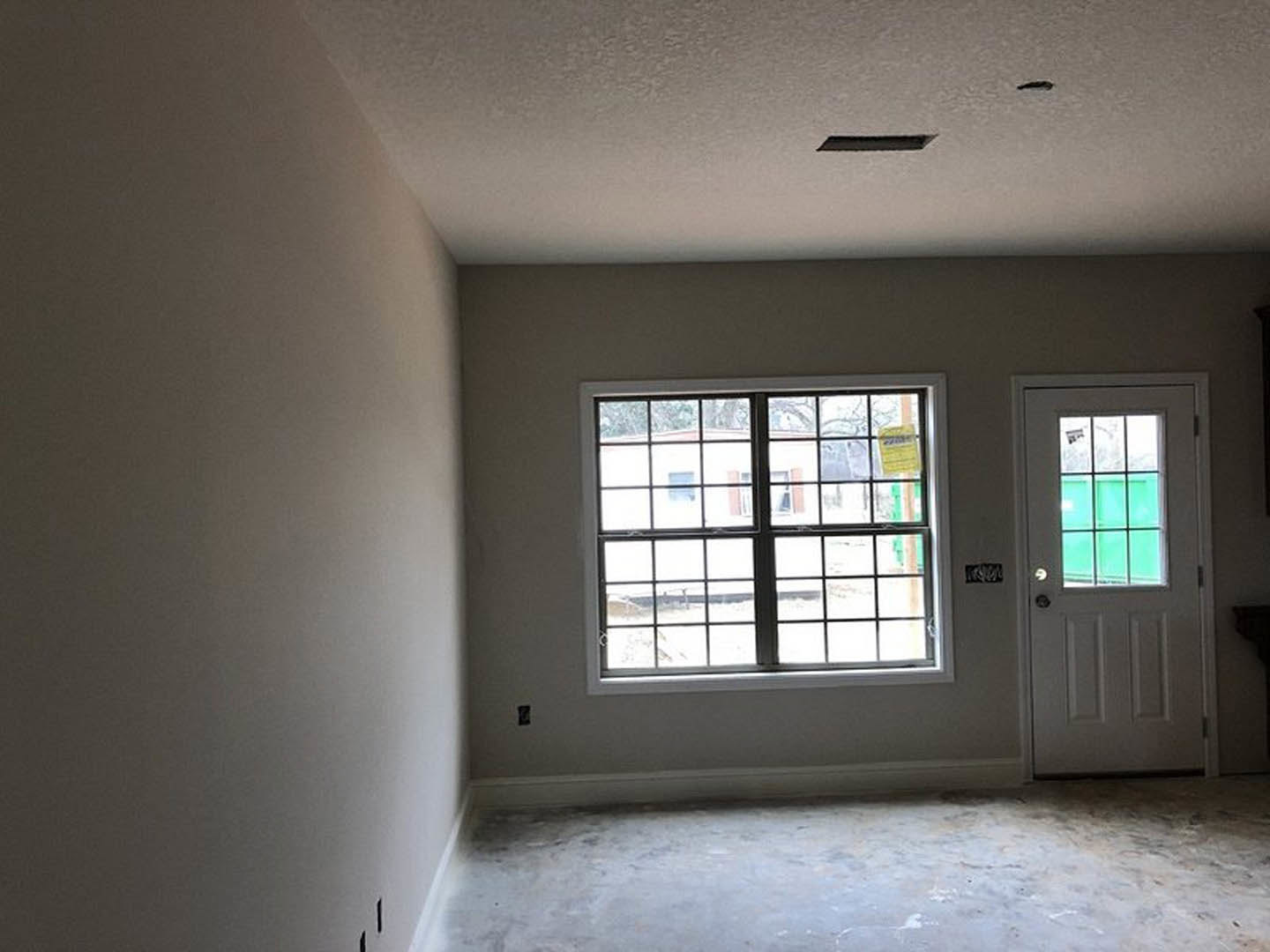 White door with glass window, large window with yellow sticker, grey plank flooring, white plaster walls, natural daylight filling the room