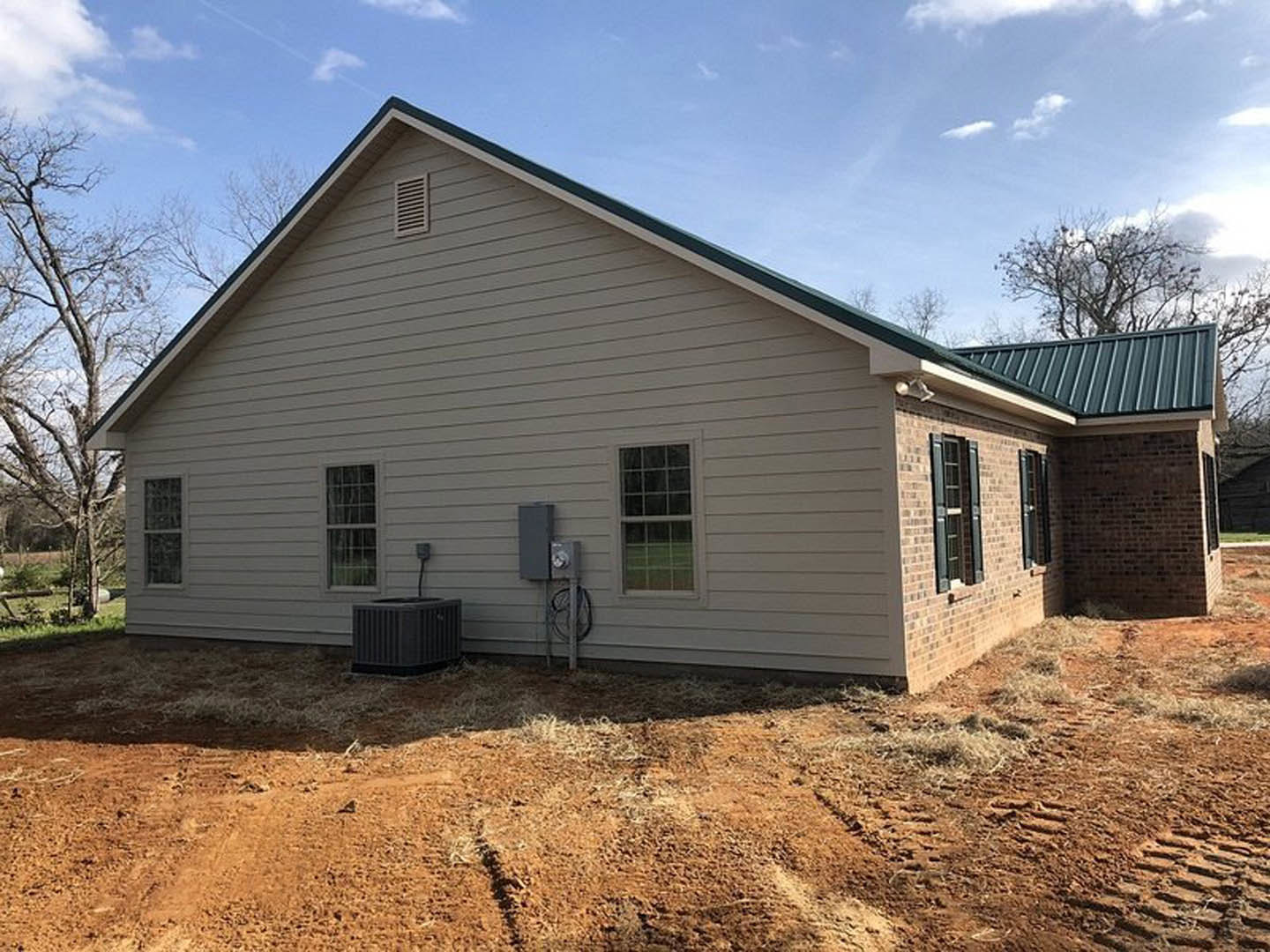 Two-story house with green metal roof, white siding, multiple-pane windows, black front door, and dirt landscaping in front.