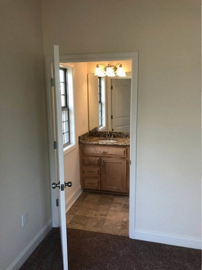 Bathroom with brown tile floor and white trim, rectangular sink with chrome faucet, large framed mirror above vanity, white cabinetry, partial view of window with metal railing.