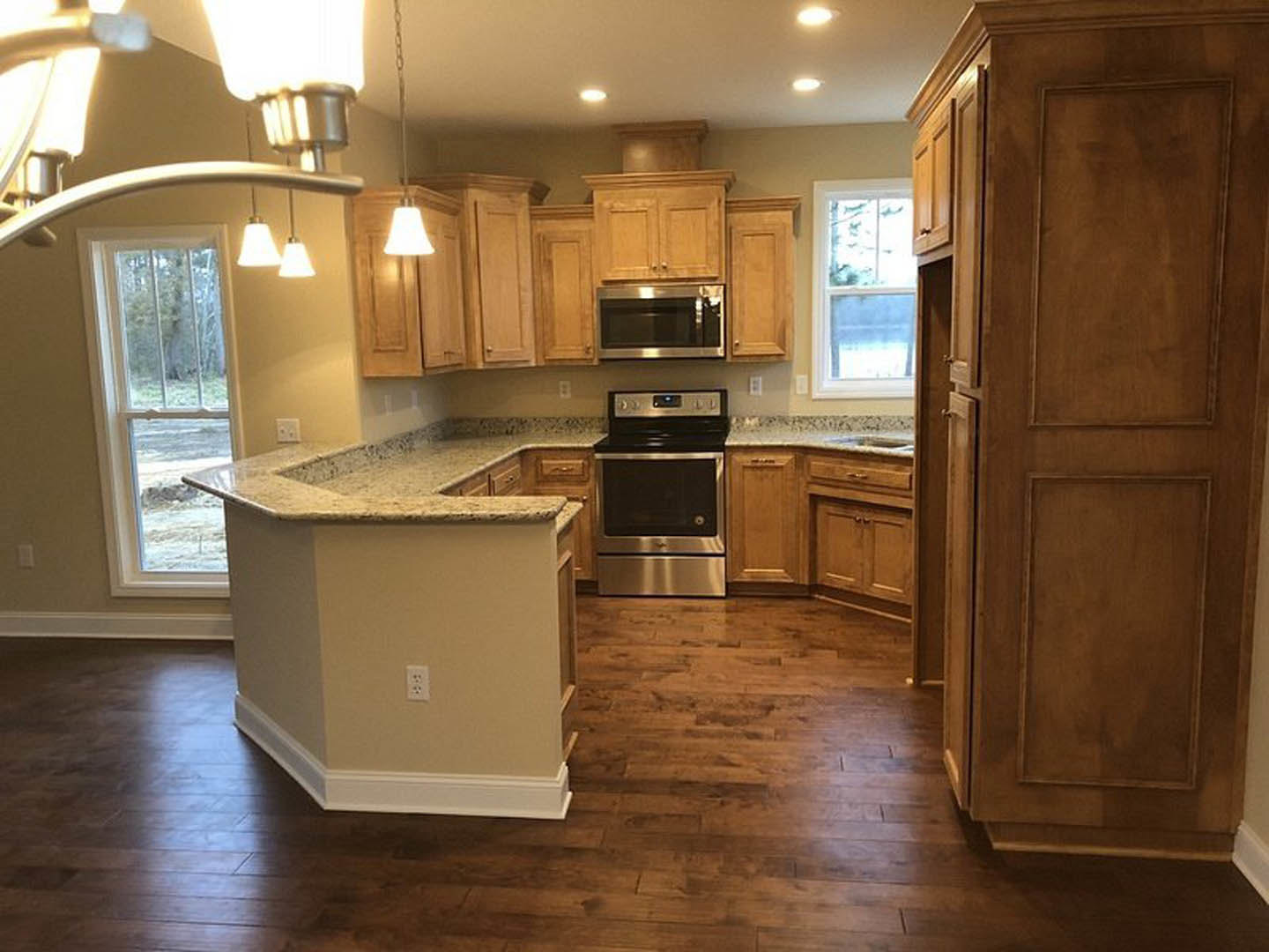 Spacious kitchen featuring a large central island with stone countertop, wide window with white frame, wooden cabinetry including an open door, and built-in microwave.