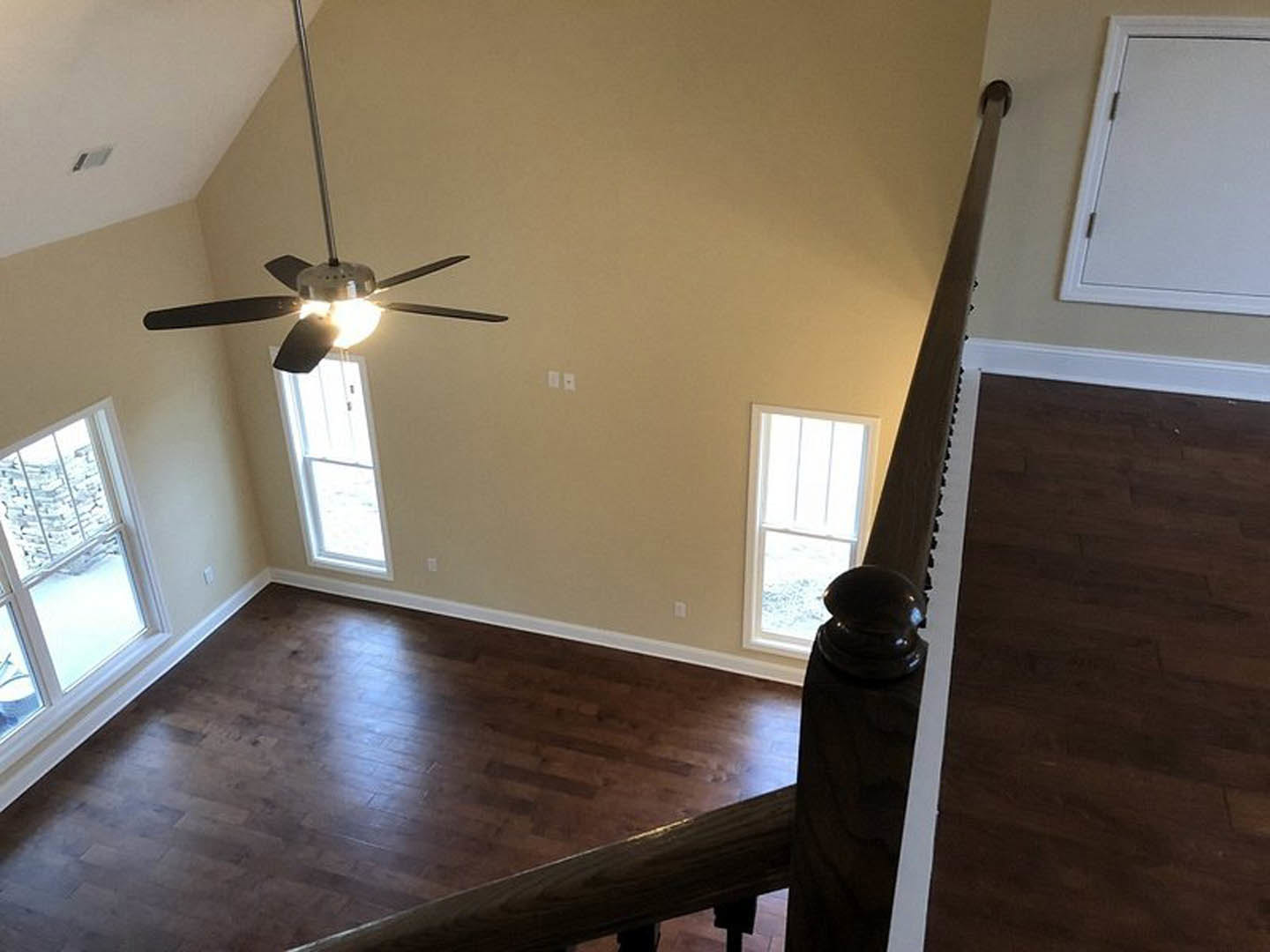 Ceiling fan with light fixture mounted on white ceiling above wood laminate flooring, white door, and window revealing exterior stone wall