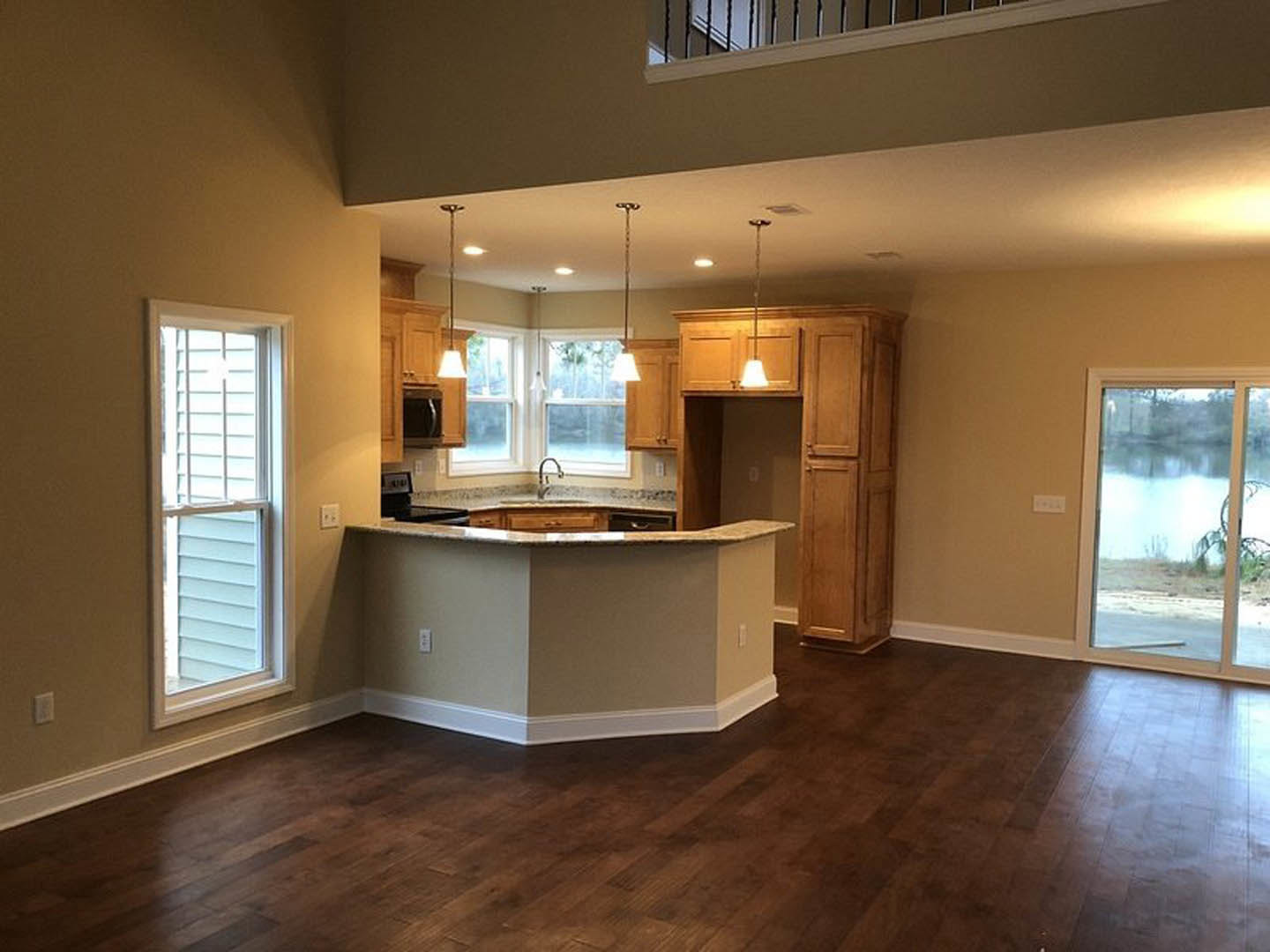 Open-concept kitchen and living room with wood flooring, white trim, cabinetry, countertops, and large windows overlooking a lake