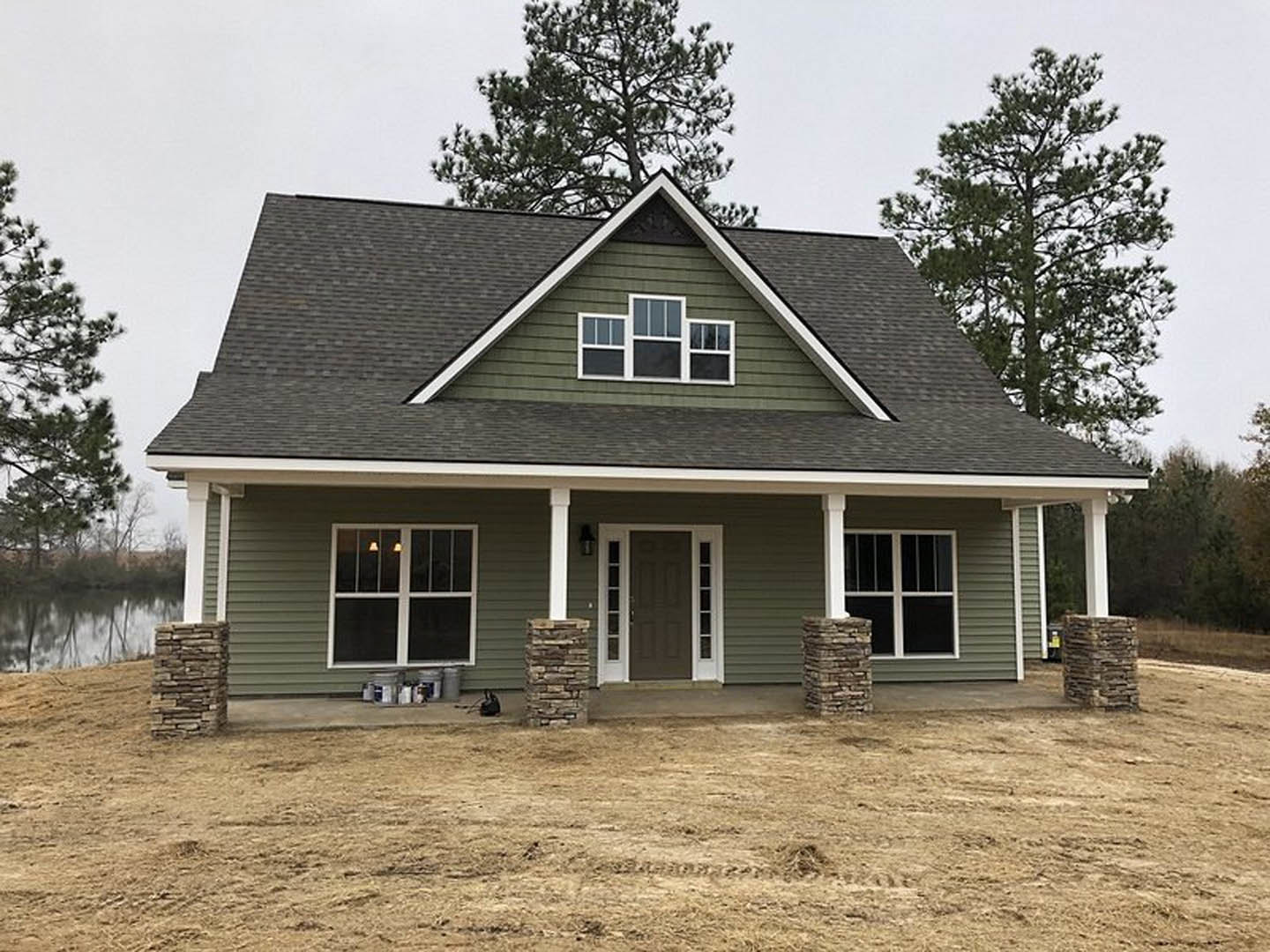 Two-story home with gray siding, stone column porch, white-trimmed door and windows, illuminated interior, large tree in backyard