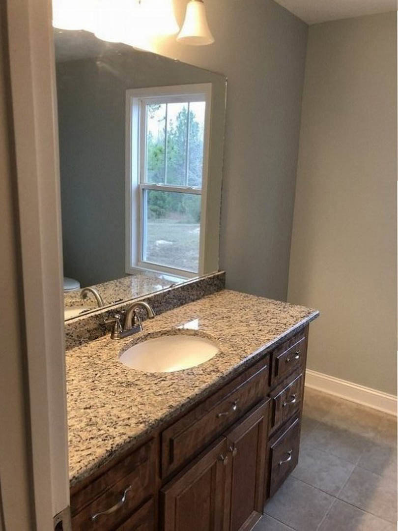 Bathroom with marble countertop sink, rectangular mirror above, tile flooring, white cabinetry, and window overlooking trees